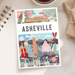 May include: A postcard featuring the word "ASHEVILLE" in bold, gray letters. The postcard has colorful illustrations of landmarks, including a banjo, a building with a flag, and a tall orange structure. A coffee cup and a notepad are in the background.