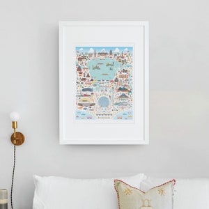May include: A framed print of a colorful illustrated map of the world with landmarks and icons representing different cities and countries. The map is surrounded by a white frame.