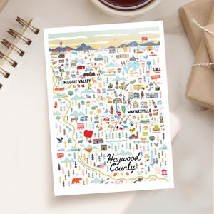 May include: A colorful illustrated map of Haywood County, North Carolina, featuring landmarks and towns like Maggie Valley and Waynesville. The map includes a scenic route, trees, and various icons, with text that reads "Haywood County".