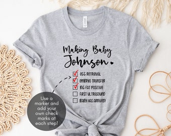 Puede incluir: Camiseta gris con el texto "Making Baby Johnson." y una lista de verificación con los siguientes elementos: "Recogida de óvulos", "Transferencia de embriones", "Positivo de embarazo", "Primera ecografía" y "¡El bebé ha llegado!" Usa un marcador para marcar cada paso.