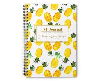 May include: A white spiral bound journal with a gold frame and the text "IVF Journal" and "Journey to Baby Johnson". The cover features a repeating pattern of yellow pineapples with green leaves on a white background.
