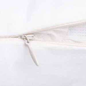 May include: Close-up of a white zipper on a pillowcase. The zipper is open and the zipper pull is white.