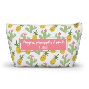 May include: White zippered pouch with a repeating pattern of yellow pineapples and green cacti. A pink rectangle in the center reads "Prayers, pineapples & pricks" with the hashtag "#IVFLIFE".