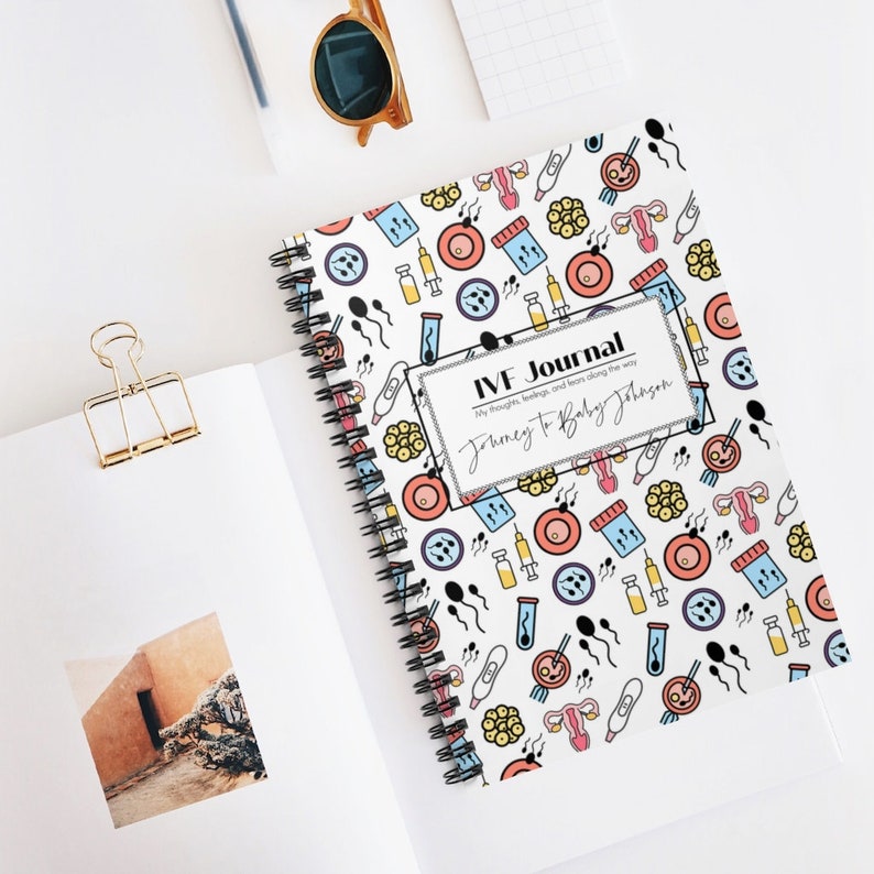 May include: A white spiral bound journal with a colorful pattern of IVF related icons. The cover has the text "IVF Journal" and "Journey to Baby Johnson".