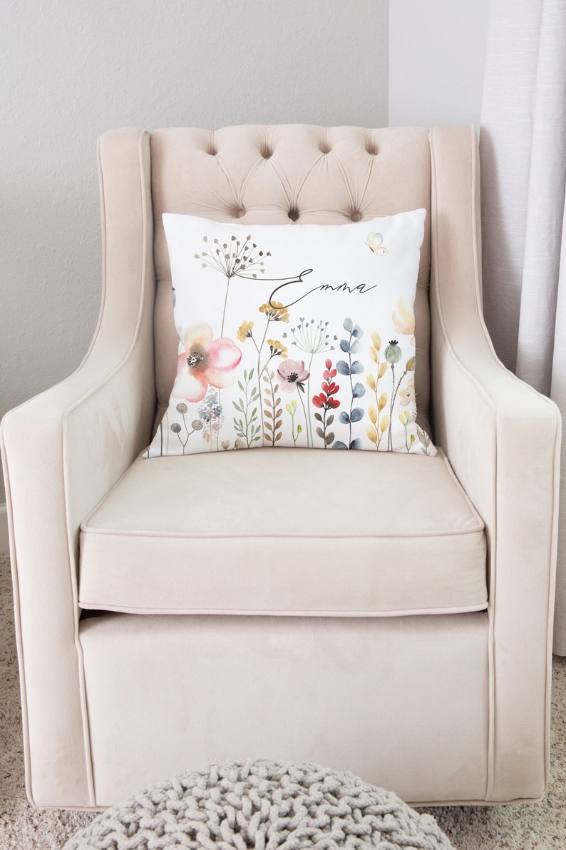 May include: A white armchair with a floral pillow featuring the name "Emma" in cursive script. The pillow has a watercolor design of flowers and leaves in shades of pink, red, blue, and yellow.