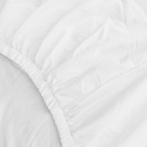 Puede incluir: Primer plano de una s&aacute;bana bajera blanca con borde el&aacute;stico. La s&aacute;bana est&aacute; hecha de una tela suave y lisa.