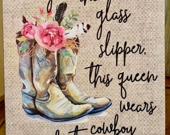 May include: A rustic brown background with white lace trim features a watercolor painting of cowboy boots with pink flowers. The text "Forget the glass slipper, this queen wears cowboy boots" is written in black cursive.