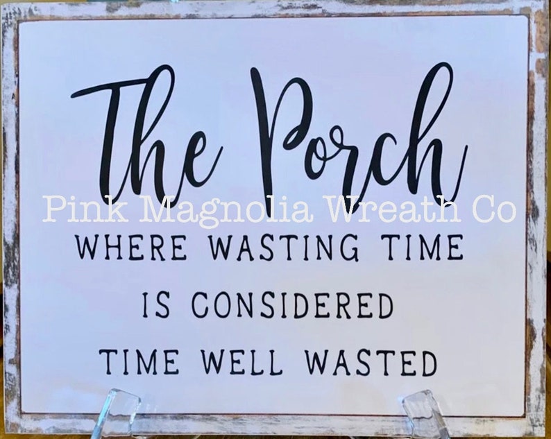 Pu&ograve; includere: Un cartello di legno bianco con testo nero che recita "The Porch Pink Magnolia Wreath Co. Where wasting time is considered time well wasted."