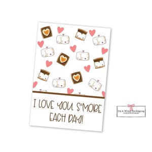 May include: A white card with a brown border and a pattern of cartoon s'mores and hearts. The text "I love you s'more each day!" is printed on the card.