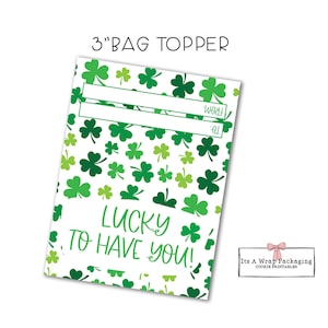 Peut inclure: Un modèle de sac imprimable de 7,6 cm avec un fond blanc et un motif de trèfles verts. Le texte "LUCKY TO HAVE YOU!" est imprimé en écriture cursive noire. Il y a deux lignes vides pour écrire "À" et "De".