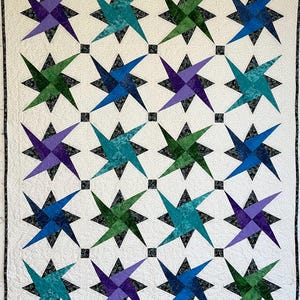 May include: A handmade quilt featuring a repeating star pattern in shades of teal, green, blue, and purple. The stars are set against a white background with a subtle dotted texture, and are separated by small black squares. The quilt is bordered with a black and white patterned fabric.