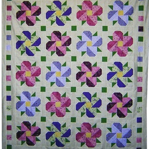 May include: A quilt with a patchwork design featuring a repeating pattern of purple, pink, and blue flowers with yellow centers. The quilt is framed with a border of green, pink, and purple squares.