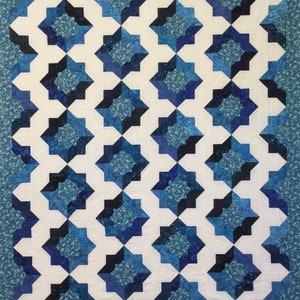 May include: A quilt with a geometric pattern of blue and white stars. The quilt is made of fabric with a subtle blue and white pattern.