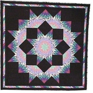 May include: A quilt with a black background and a large, multi-colored starburst pattern in shades of pink, purple, and green.