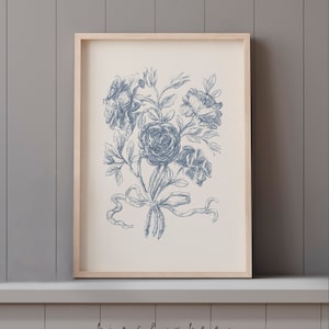 Puede incluir: Una impresi&oacute;n enmarcada de una ilustraci&oacute;n floral azul y blanca. La ilustraci&oacute;n presenta un ramo de rosas atadas con una cinta. La impresi&oacute;n est&aacute; sobre un fondo blanco y est&aacute; enmarcada en un marco de madera natural.
