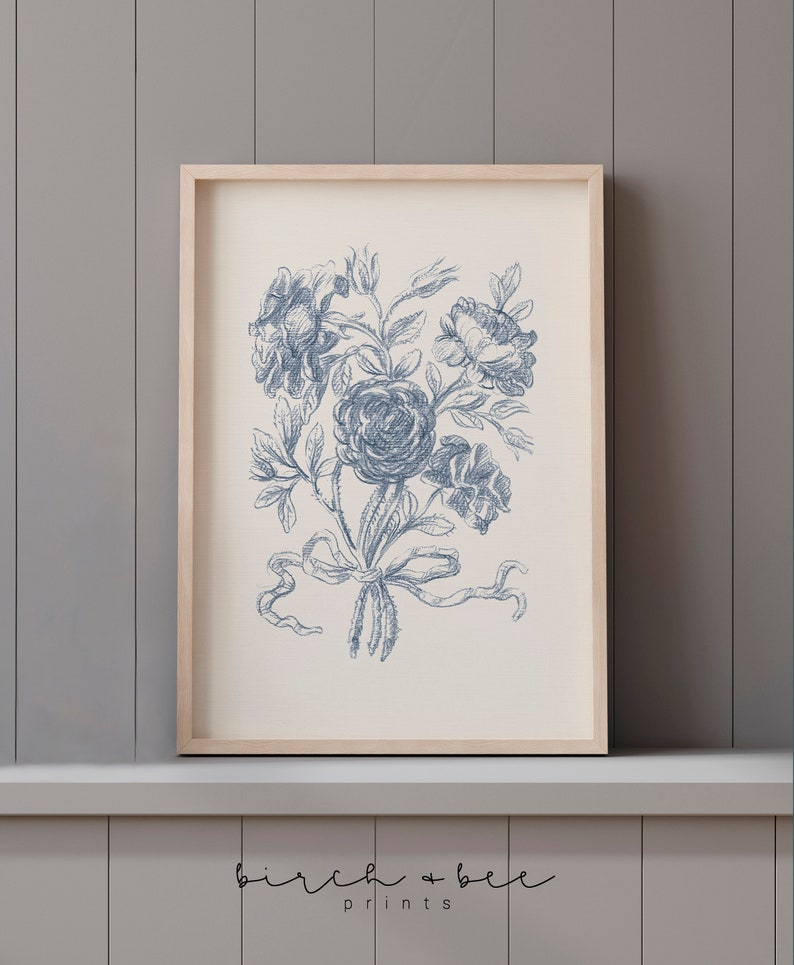 Puede incluir: Una impresi&oacute;n enmarcada de una ilustraci&oacute;n floral azul y blanca. La ilustraci&oacute;n presenta un ramo de rosas atadas con una cinta. La impresi&oacute;n est&aacute; sobre un fondo blanco y est&aacute; enmarcada en un marco de madera natural.
