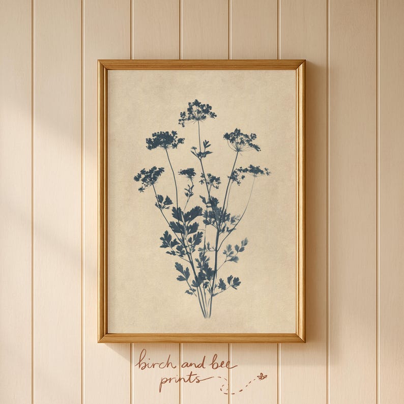 Puede incluir: Una l&aacute;mina de arte mural enmarcada que presenta una ilustraci&oacute;n bot&aacute;nica en azul oscuro de un grupo de flores silvestres sobre un fondo beige claro texturizado. La obra est&aacute; en un marco fino de metal dorado y muestra una silueta vegetal detallada.