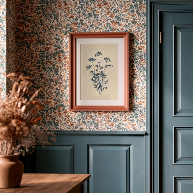 Puede incluir: Un marco de fotos rectangular montado en la pared con un borde de color terracota que contiene una impresi&oacute;n bot&aacute;nica de una ilustraci&oacute;n de planta azul oscuro sobre un fondo crema, exhibido en una pared con papel tapiz floral y friso azul.