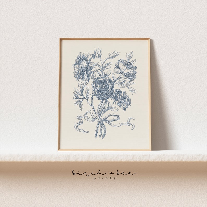 Puede incluir: Una impresi&oacute;n floral vintage azul y blanca con un ramo de rosas atado con una cinta. La impresi&oacute;n est&aacute; enmarcada en un marco de madera claro.