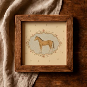 May include: A square wooden frame containing a print of a light brown horse standing in profile. The horse is centered within an ornate, scalloped border featuring small pink flowers against a cream background with a repeating floral pattern.
