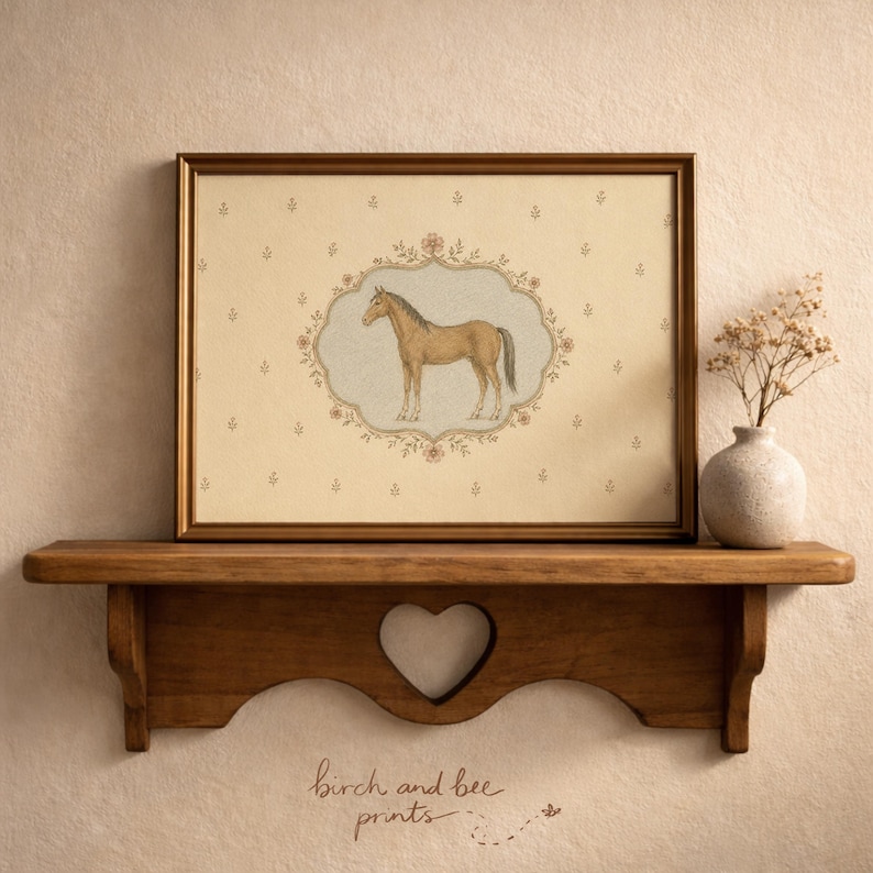 May include: A framed print featuring a brown horse illustration inside an ornate floral oval border on a cream background with small flower motifs. The print is displayed on a wooden shelf with a heart-shaped cutout, next to a small ceramic vase.