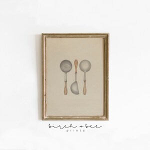 May include: A framed print of a watercolor illustration of three vintage kitchen ladles with wooden handles. The ladles are arranged vertically in a row. The background is a light beige color. The print is framed in a gold-colored frame.