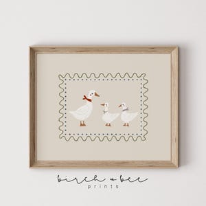 K&ouml;nnte beinhalten: Ein beiger druckbarer Kunstdruck mit einem gr&uuml;nen und blauen Rand, der drei wei&szlig;e Enten mit roten und violetten Akzenten zeigt. Der Druck hat den Text "birch + bee prints" unten.