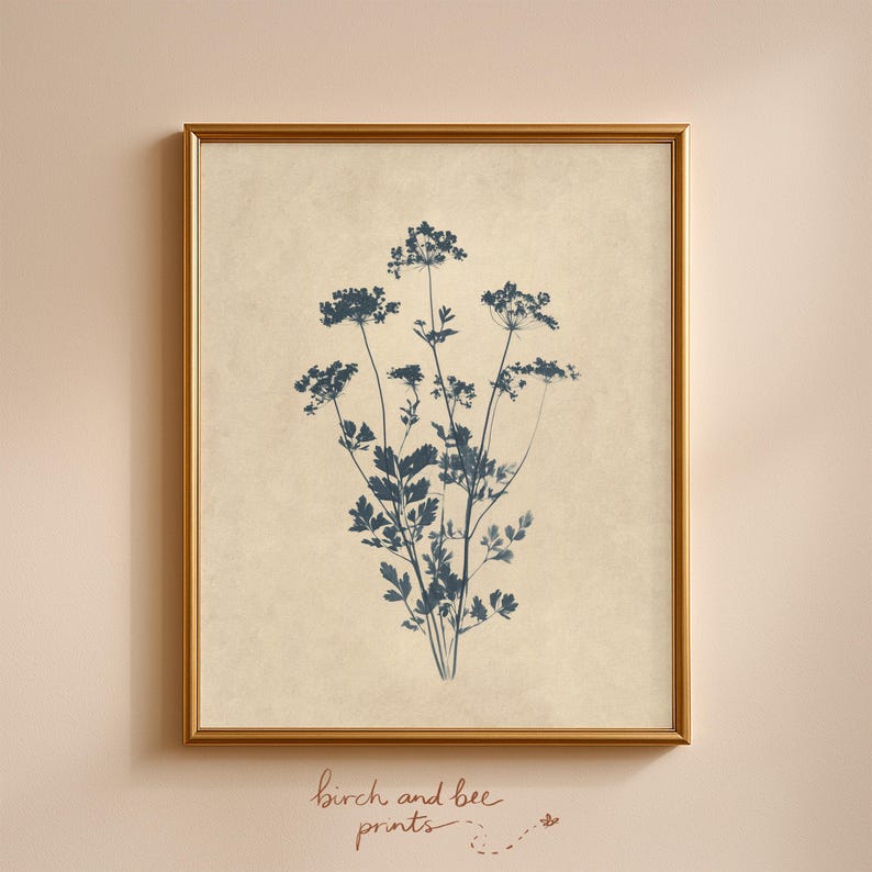 Puede incluir: Una impresi&oacute;n de arte mural enmarcada que presenta una ilustraci&oacute;n bot&aacute;nica azul oscuro de flores silvestres sobre un fondo beige texturizado. La obra est&aacute; encerrada en un marco dorado fino. Debajo del marco, el texto dice birch and bee prints.