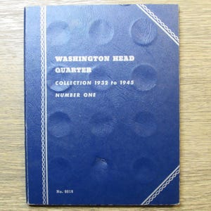 May include: A blue coin collection album titled "Washington Head Quarter Collection 1932 to 1945 Number One." The cover has a textured surface with embossed circles and white decorative trim. The album is on a wooden surface.