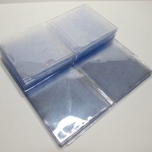 K&ouml;nnte beinhalten: Ein Stapel klarer, quadratischer Kunststoffh&uuml;llen, wahrscheinlich zur Aufbewahrung von Karten oder Fotos. Die H&uuml;llen sind transparent und erm&ouml;glichen die Sichtbarkeit des Inhalts. Das Bild ist aus leicht erh&ouml;hter Perspektive aufgenommen und zeigt den Stapel und einige einzelne H&uuml;llen.