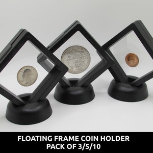 Puede incluir: Tres marcos flotantes negros de forma cuadrada para monedas, cada uno con una ventana transparente que muestra una moneda diferente. Los marcos están sobre bases negras. El texto en la parte inferior dice "FLOATING FRAME COIN HOLDER PACK OF 3/5/10".
