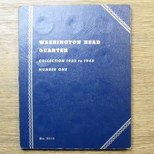 May include: A blue coin collection album titled "Washington Head Quarter Collection 1932 to 1945 Number One." The cover has white decorative trim and the number "No. 9018" at the bottom. The album is on a light wood surface.