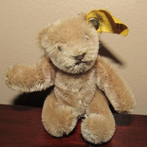 Pode incluir: Um pequeno urso de peluche de mohair castanho com uma etiqueta amarela que diz "Made in Germany".