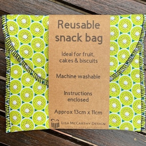 May include: A reusable snack bag with a kiwi fruit pattern. The bag is made of fabric and has a brown label that says "Reusable snack bag", "Ideal for fruit, cakes & biscuits", "Machine washable", "Instructions enclosed", "Approx 13cm x 11cm", "LISA MCCARTHY DESIGN", "GIFTS TO MAKE YOU SMILE".