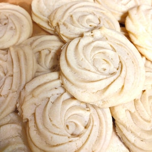 May include: A close-up of a pile of shortbread cookies. The cookies are light brown and have a swirl pattern. They are arranged in a random pattern.