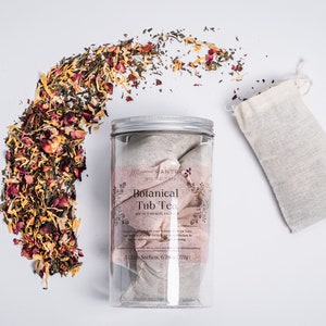 May include: A clear plastic jar with a silver lid containing Botanical Tub Tea sachets. Dried herbs and flower petals are scattered around the jar. A small, off-white linen bag sits to the right. The label reads "Botanical Tub Tea".