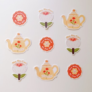 Könnte beinhalten: Neun bunte Aufkleber mit motivierenden Botschaften und Illustrationen. Die Aufkleber zeigen eine Teekanne, eine Blume und eine Sonne mit einem lächelnden Gesicht. Der Text auf den Aufklebern lautet "You Believed So You Did", "Yes, You Can" und "It's a Beautiful Life".