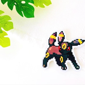 Könnte beinhalten: Ein schwarzer und roter pixelartiger Pokémon-Charakter mit gelben Akzenten. Der Charakter steht auf einem weißen Hintergrund.