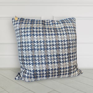 May include: A blue and beige patterned throw pillow with a zipper closure. The pillow is on a white tiled floor.