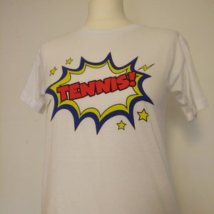 May include: White t-shirt with a red, yellow, and blue comic book style graphic that says "TENNIS!"