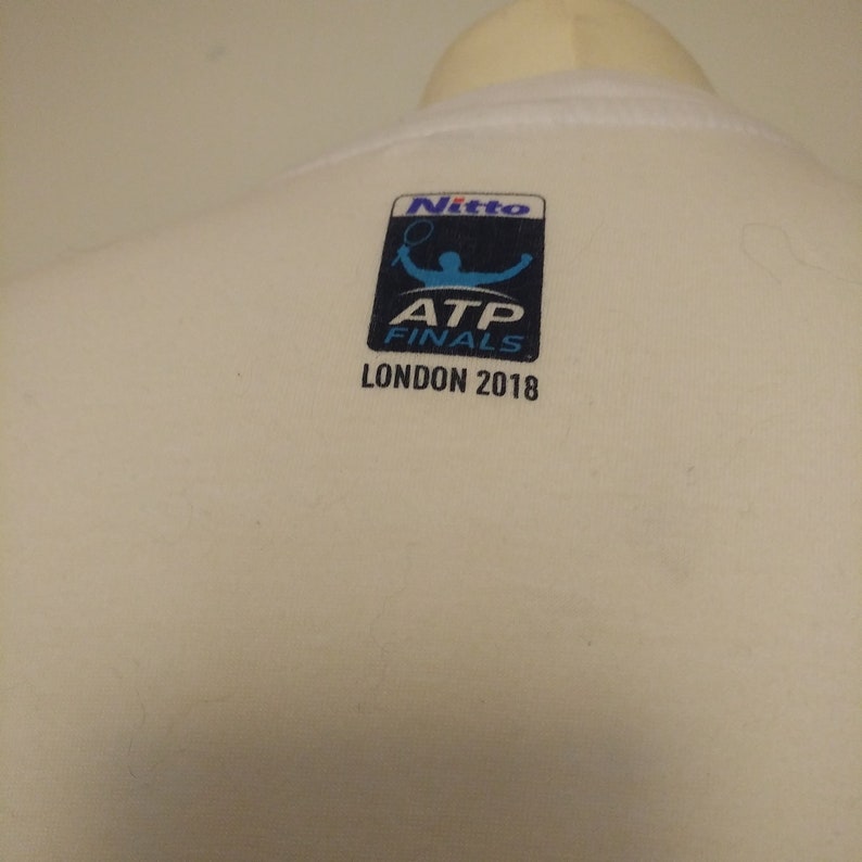 May include: White t-shirt with a blue and white logo that says "Nitto ATP Finals London 2018".