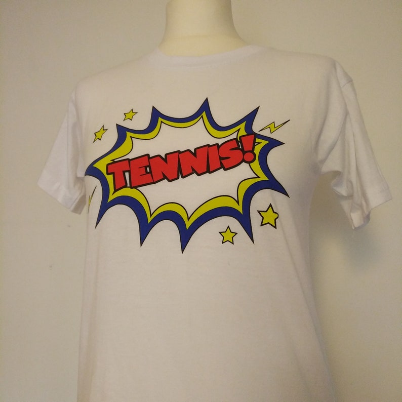 May include: White t-shirt with a red, yellow, and blue comic book style graphic that says "TENNIS!"