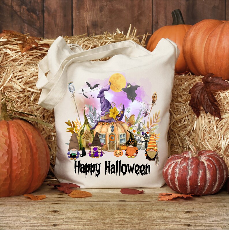 Pu&ograve; includere: Una borsa tote in tela bianca con un design a tema Halloween. Il design presenta una casa a forma di zucca con un cappello da strega, gnomi e il testo "Happy Halloween".