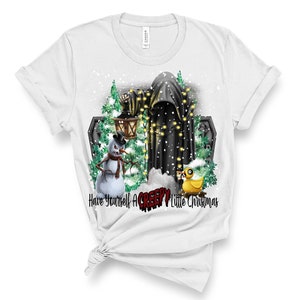 Op de afbeelding: Wit T-shirt met een afbeelding van een griezelige sneeuwpop, een geest met kerstverlichting en een rubberen eend. De tekst "Have Yourself A CREEPY Little Christmas" is onder de afbeelding gedrukt.
