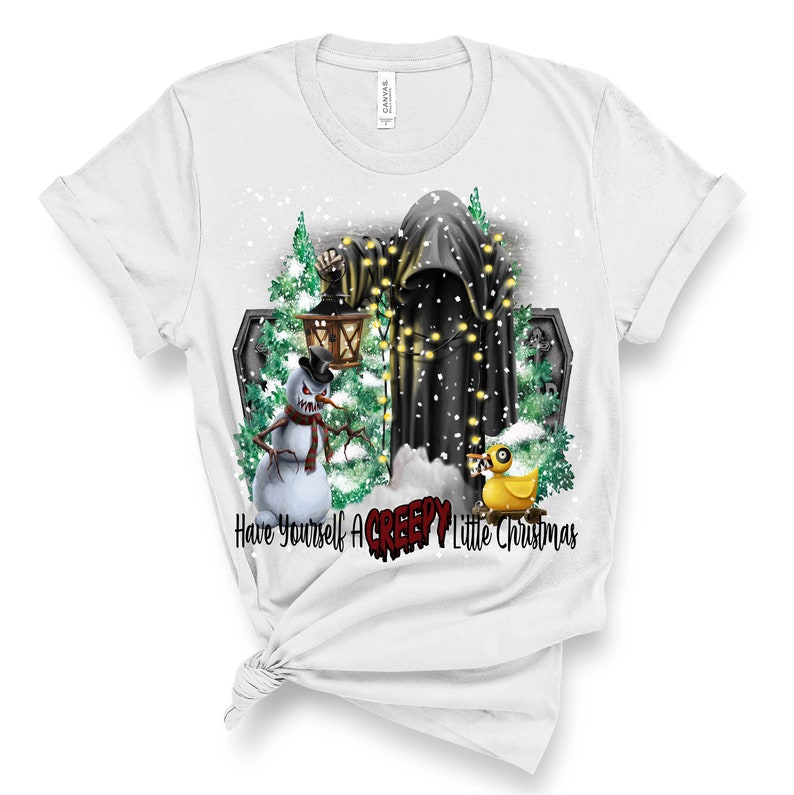 Op de afbeelding: Wit T-shirt met een afbeelding van een griezelige sneeuwpop, een geest met kerstverlichting en een rubberen eend. De tekst "Have Yourself A CREEPY Little Christmas" is onder de afbeelding gedrukt.