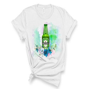 May include: White t-shirt featuring a green Heineken beer bottle design with a floral arrangement. The bottle has a green label with the Heineken logo. The design is set against a watercolor background.