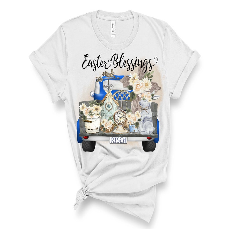 Peut inclure: T-shirt blanc avec un plateau de camion bleu rempli de d&eacute;corations de P&acirc;ques, dont une croix, un nichoir, une horloge, un seau et un lapin. Le texte "Easter Blessings" est au-dessus du camion et "RISEN" est sur la plaque d'immatriculation.