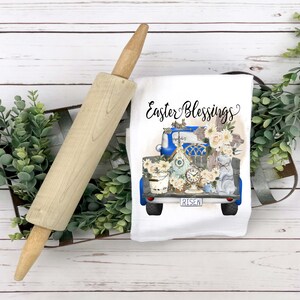 Peut inclure: Une serviette de cuisine blanche avec un camion bleu transportant une maison d'oiseau, une horloge, un seau et des fleurs. Le camion a le mot "RISEN" sur la plaque d'immatriculation. Le texte "Easter Blessings" est &eacute;crit au-dessus du camion.