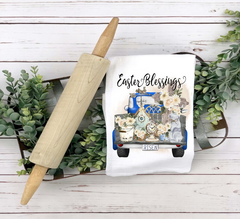 Peut inclure: Une serviette de cuisine blanche avec un camion bleu transportant une maison d'oiseau, une horloge, un seau et des fleurs. Le camion a le mot "RISEN" sur la plaque d'immatriculation. Le texte "Easter Blessings" est &eacute;crit au-dessus du camion.