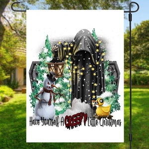 Op de afbeelding: Een witte tuin vlag met een zwarte gekapte figuur, een sneeuwpop met een dreigende grijns, een gele rubberen eend en een lantaarn. De tekst luidt "Have Yourself A Creepy Little Christmas".